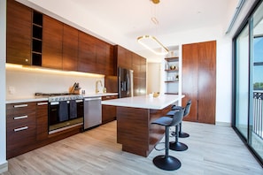 A modern kitchen with wooden cabinets, a stainless steel refrigerator, and a bar area with stools. - Ocean-view terrace, Pool & BBQ, Conchas Chinas (Puerto Vallarta)
