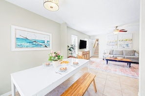 A dining area with a long white table, a bench, and a potted plant.