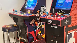 Dues màquines recreatives, una amb la inscripció "X-Men" i l'altra "NBA JAM", amb un tamboret al davant.
