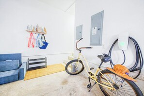 A room with a bicycle, a charging station, a blue sofa, and a shelf with bags.