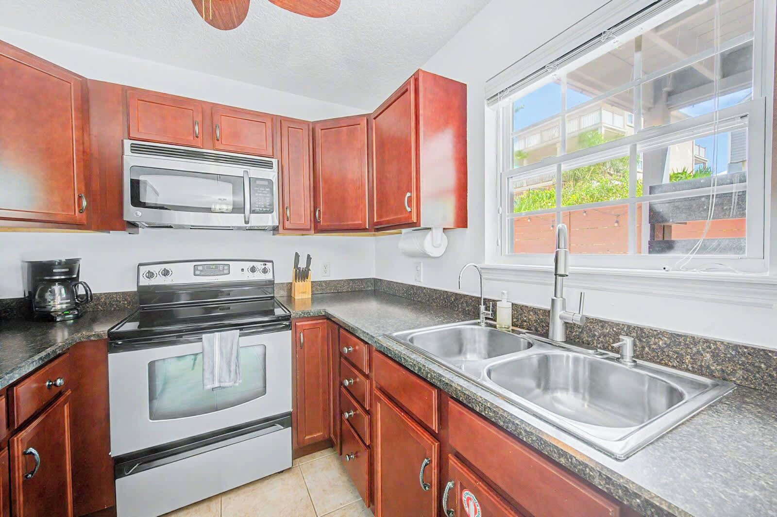A kitchen with wooden cabinets, a stainless steel sink, a double oven, and a window with a view of greenery.