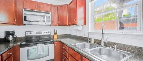 A kitchen with wooden cabinets, a stainless steel sink, a double oven, and a window with a view of greenery.