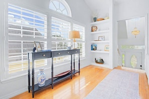 A room with a wooden floor, a table with a lamp, a vase, and shelves with decorative items.