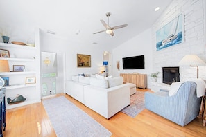 A modern living room with a white sofa, a television, a fireplace, and a ceiling fan.