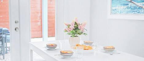 A dining area with a white table set for four, a vase with flowers, and a painting on the wall.