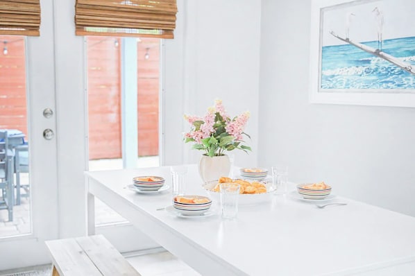 A dining area with a white table set for four, a vase with flowers, and a painting on the wall.