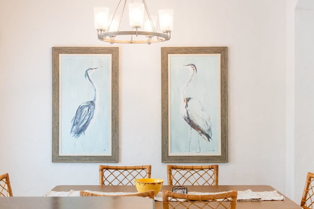 Uma sala de jantar com uma mesa, cadeiras e dois quadros de pássaros na parede.