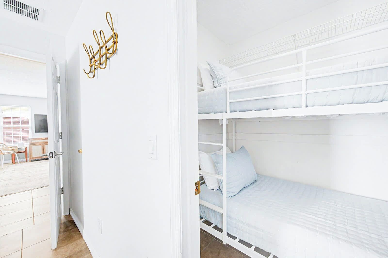 A white interior with a bunk bed, a door with a golden handle, and a white wall with a simple light switch.