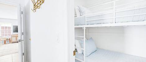 A white interior with a bunk bed, a door with a golden handle, and a white wall with a simple light switch.