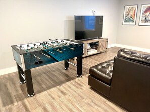 A living room with a foosball table, a television, and a leather couch.