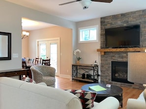 A living room with a fireplace, a television, and a dining area in the background.