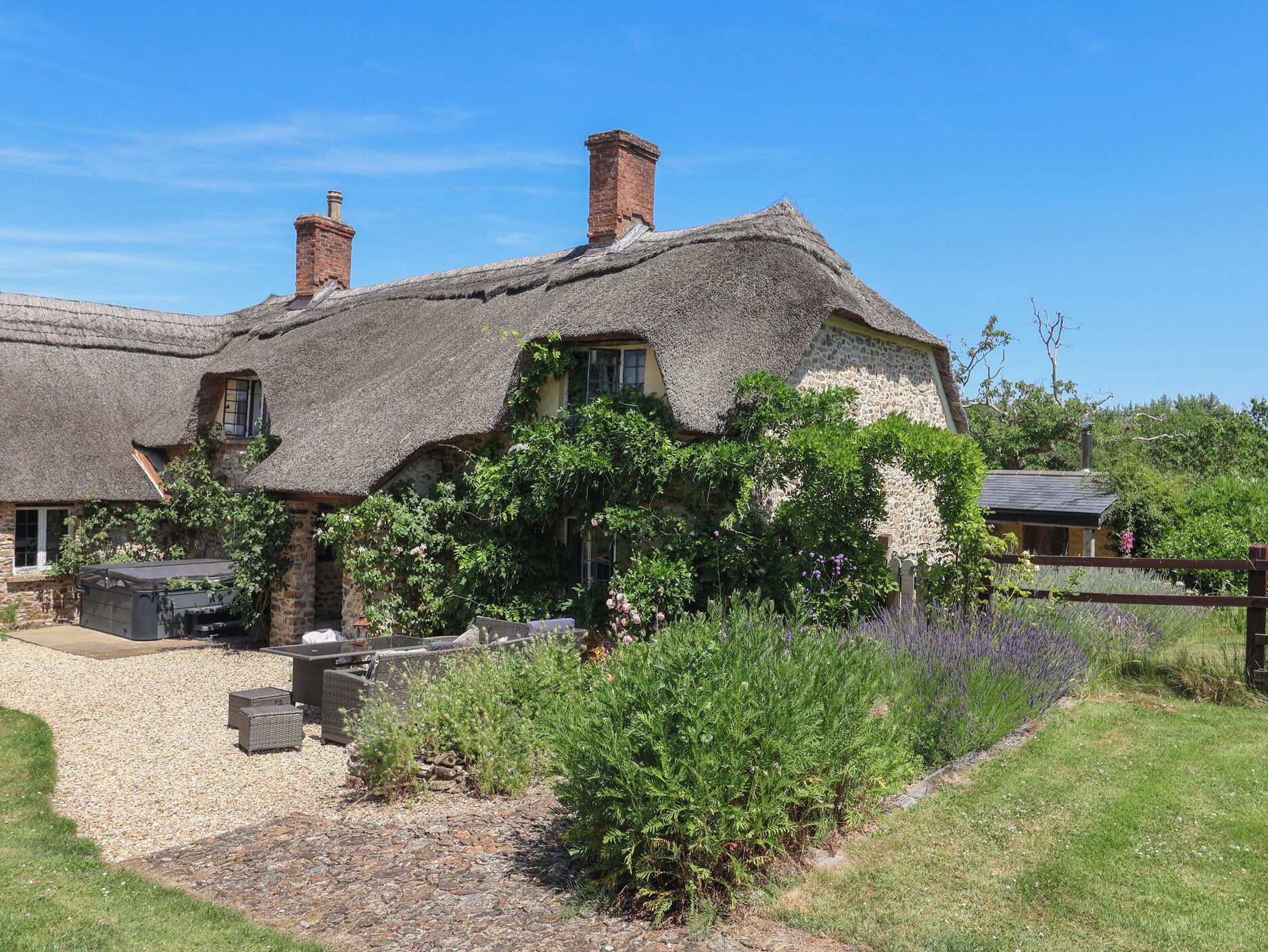 A thatched-roof cottage with stone walls, a gravel driveway, and surrounding greenery.