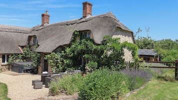 Un charmant cottage à toit de chaume, aux murs en pierre, avec une allée gravillonnée et entouré de verdure.