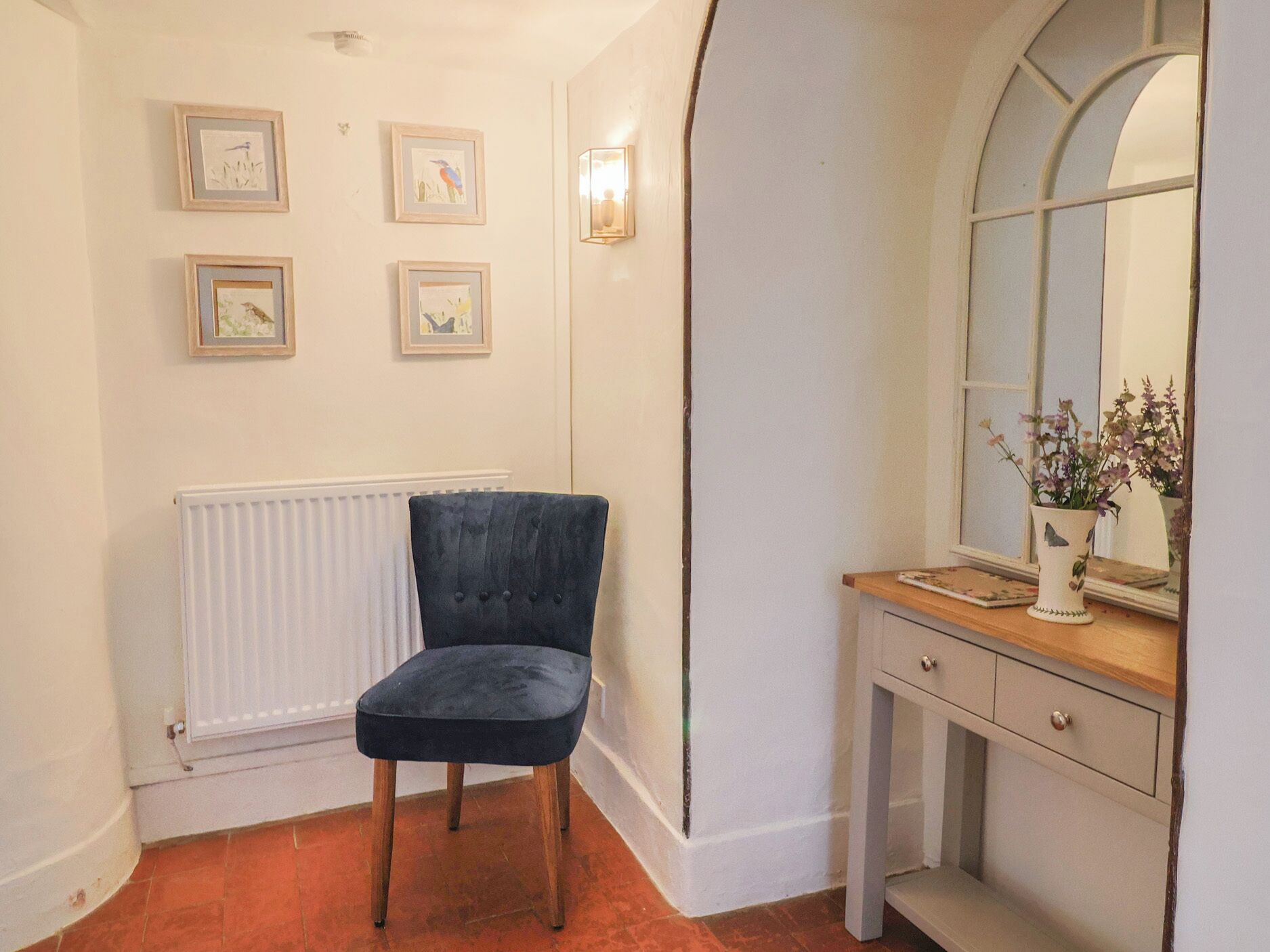 A room with a dark blue chair, a white radiator, and a small table with a vase of flowers.