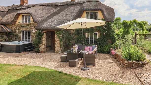 A thatched-roof house with a hot tub, outdoor seating, and a garden. - Garden View (Wellington)