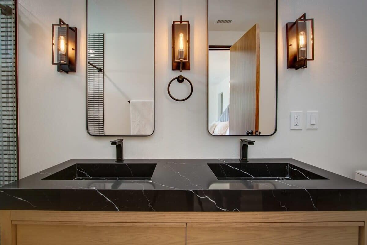 A modern bathroom with two sinks, marble countertops, and wall-mounted mirrors with light fixtures.