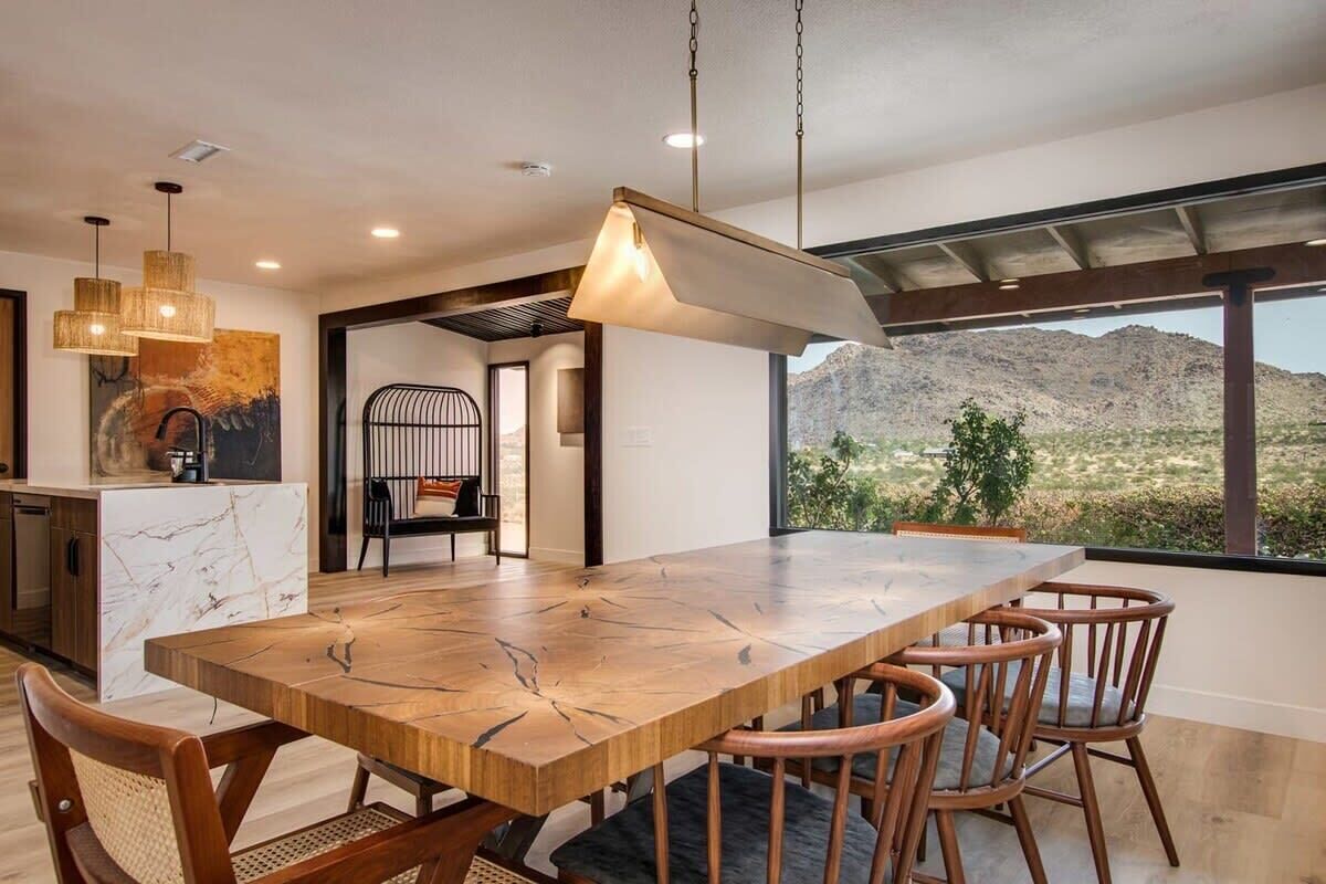 Un comedor amplio con una gran mesa de madera y seis sillas, una cocina moderna con encimeras de mármol y vistas a las montañas a través de amplios ventanales.