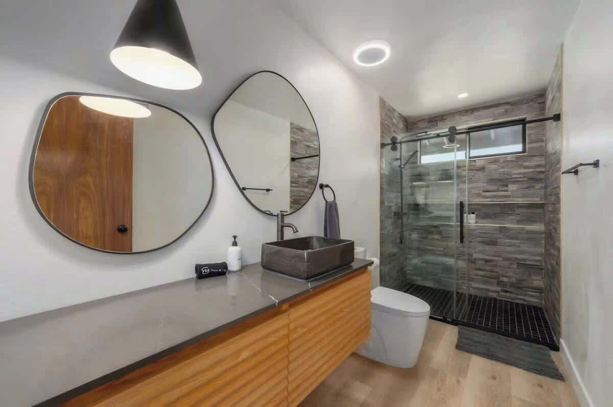 A modern bathroom with a wooden vanity, two mirrors, a glass shower enclosure, and a built-in sink.