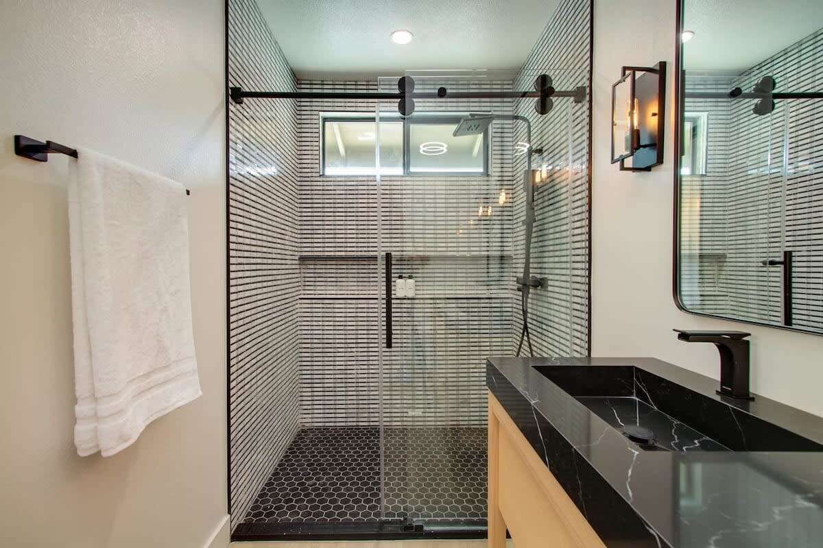 Een moderne badkamer met een douchecabine van glas, een zwart marmeren wastafel en een grote spiegel.