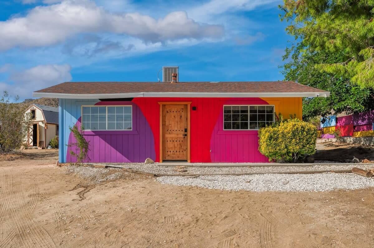 A colorful house with a red door, purple and blue walls, and a gravel driveway.