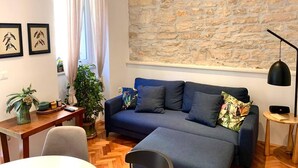 A modern living room with a stone wall, a blue sofa, a wooden table, and a potted plant. - City Center Appartment Near Arena-pula (Pula)