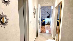 A hallway with a wooden stool, a mirror, and a door leading to a room with a blue sofa and a stone wall. - City Center Appartment Near Arena-pula (Pula)