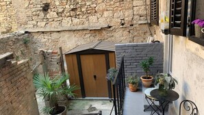 A narrow courtyard with a wooden door, potted plants, a small table, and a chair. - City Center Appartment Near Arena-pula (Pula)