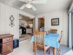 Un comedor con mantel azul, sillas de madera, un ventilador de techo y una cocina al fondo.
