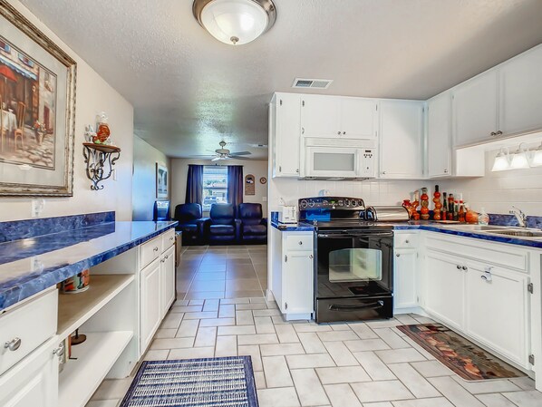Una cocina con armarios blancos, microondas, estufa y comedor con encimera azul y sillas.