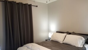 A bedroom with a bed, white and brown bedding, a nightstand with a lamp, and a window with curtains.