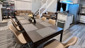 A modern kitchen with a built-in stove, a dining area with a long table and chairs, and a staircase leading to an upper level. - Luxury Mountain Home 5BD/3BA, AC, 3 Min to Pool, Near Major Pocono Attractions. (Tobyhanna)