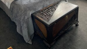 A hotel room with a bed, a wooden chest of drawers, a small table, and a window with curtains. - Peaky Blinder themed hotel rooms/studio apartments (Dudley)