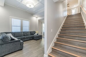 Relax in this spacious living area with a sofa, large window, and staircase leading to an upper level.