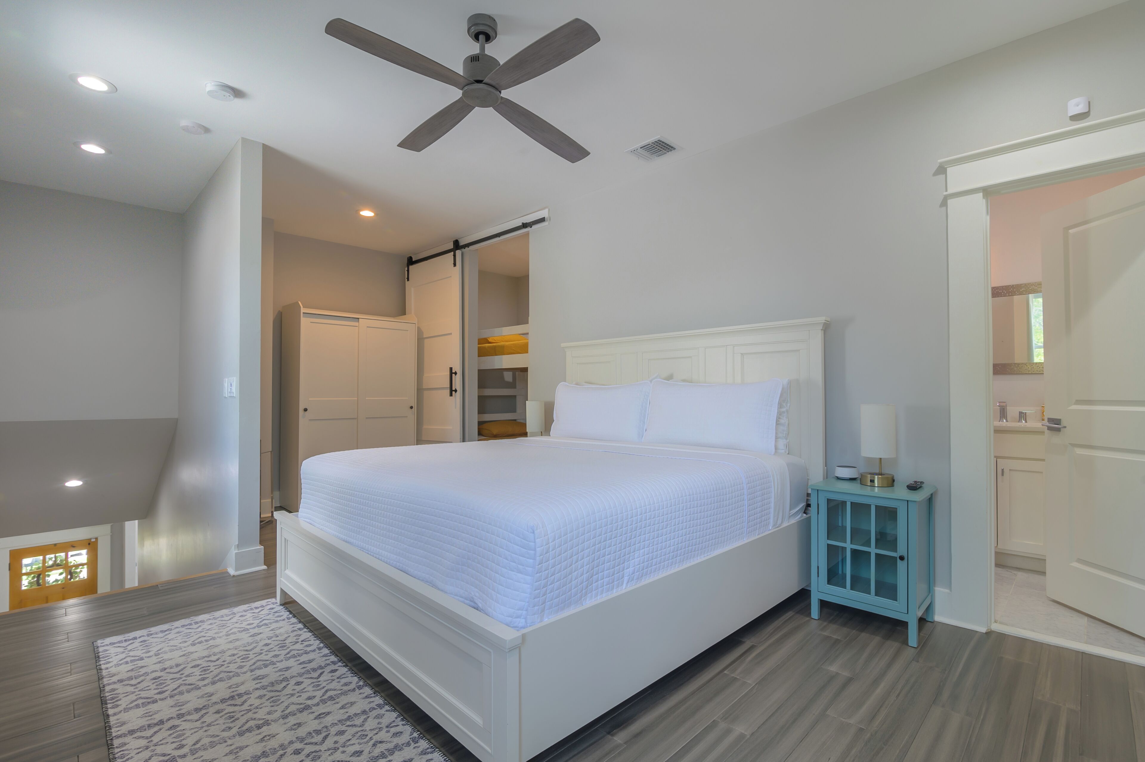 A bedroom with a bed, a ceiling fan, a nightstand, and a door leading to another room.