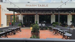 An outdoor patio area with tables and chairs, a sign reading "PHARM TABLE", and a brick floor.