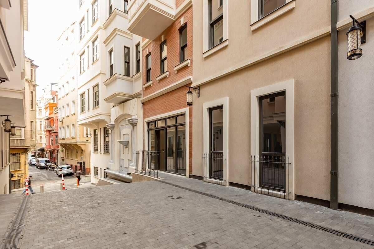 A narrow urban street with multi-story buildings, a paved sidewalk, and a few parked cars.