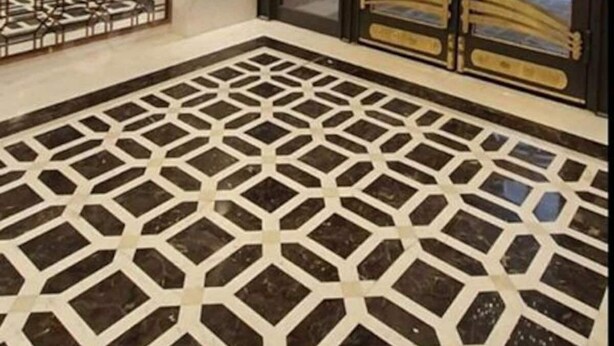 Ein modernes Interieur mit einem geometrisch gemusterten Boden, einer dekorativen Metallwand und einer Glastür mit Metallrahmen.