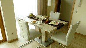 Comedor con mesa preparada para dos personas, destacando una mesa de color claro, sillas blancas y una bandeja con comida y bebidas.