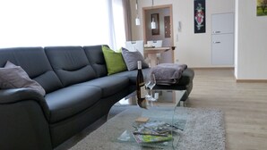 Una sala de estar moderna con un sofá negro, una mesa de centro de vidrio y una zona de comedor al fondo.