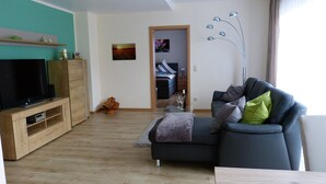 Una sala de estar moderna con un televisor de pantalla plana, un mueble de entretenimiento de madera y un sofá oscuro con cojines.
