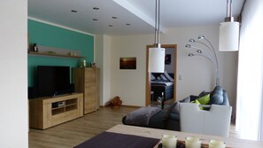 A modern living room with a TV, wooden entertainment unit, and a dining area with candles.