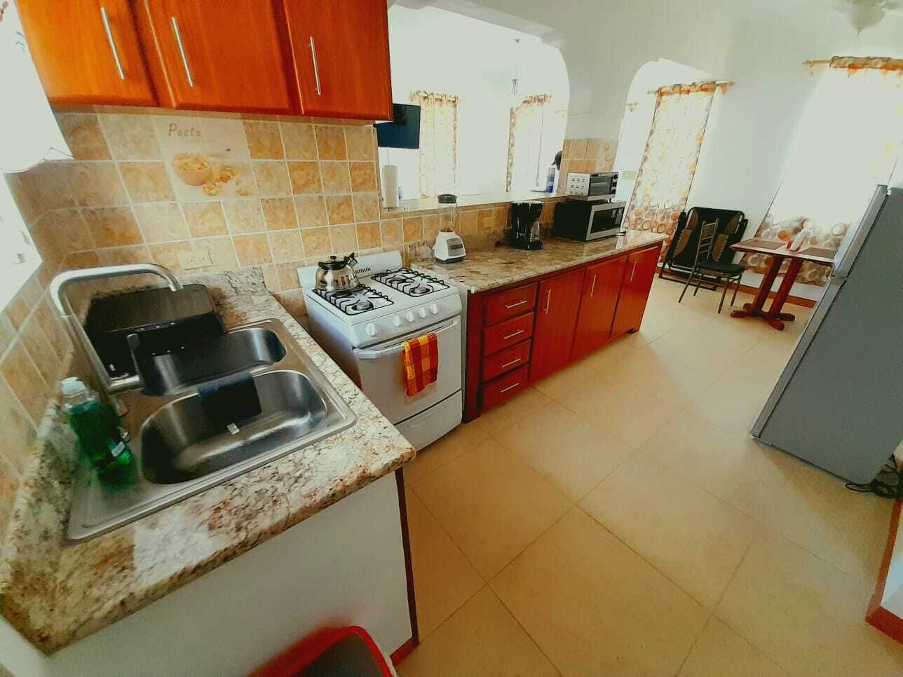 Une cuisine de taille réduite, équipée d’une cuisinière à gaz, d’un évier et de placards rouges.