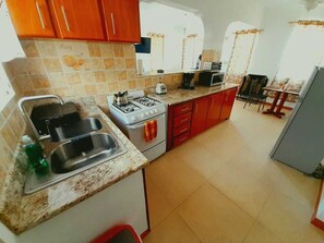 Une cuisine de taille réduite, équipée d’une cuisinière à gaz, d’un évier et de placards rouges.