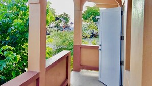 Un couloir avec une porte blanche, des murs de couleur beige et une vue sur la verdure à l’extérieur.