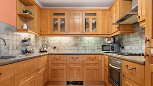A kitchen with wooden cabinets, a microwave, a kettle, and a stove. - Arcadia House - Close to Beaches, Harbour and Town (Tenby)