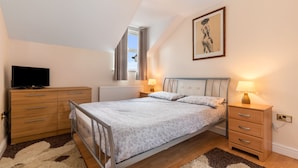 A bedroom with a bed, bedside tables, a TV, a radiator, and a window with curtains. - Arcadia House - Close to Beaches, Harbour and Town (Tenby)