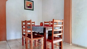 Un comedor con mesa y sillas de madera, suelo de baldosas y un cuadro enmarcado en la pared.