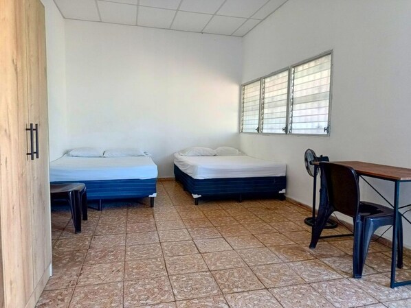 A small, clean room with two beds, a desk, and a chair.