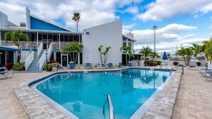 A swimming pool with a clear blue water, surrounded by a brick deck and a building with a white facade and blue accents.