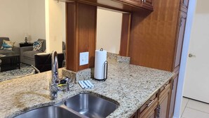 A kitchen with granite countertops, stainless steel sinks, wooden cabinets, and a paper towel dispenser.